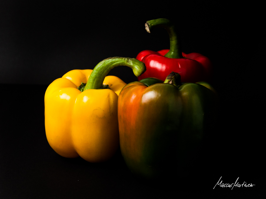 Gelbe, rote und grüne Paprika im hellen Licht vor schwarzem Hintergrund